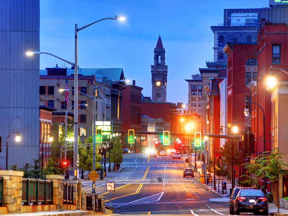 A picture of a city street leading up to an illuminated bell tower at night