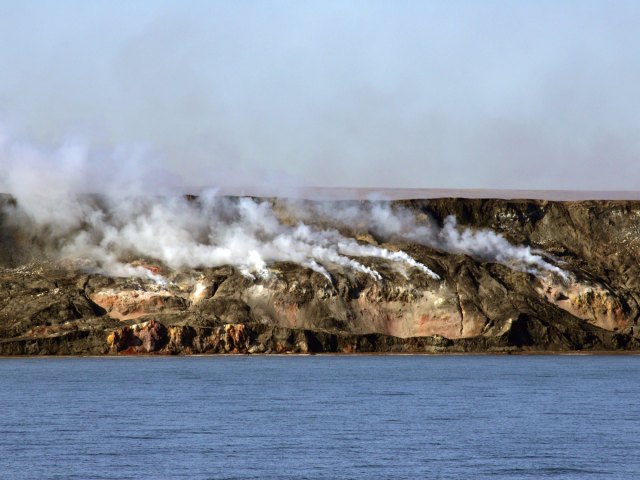 Smoke emitting from hills in the Northwest Territories of Canada, seen from across bay