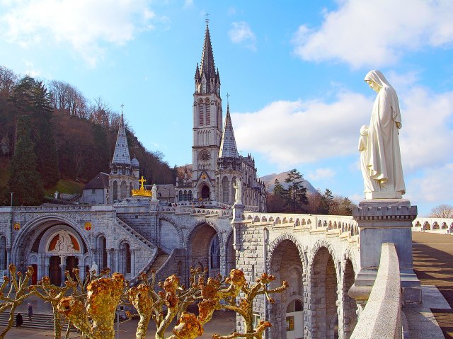 Statue of holy figure on bridge leading to church tower in Lourdes, France