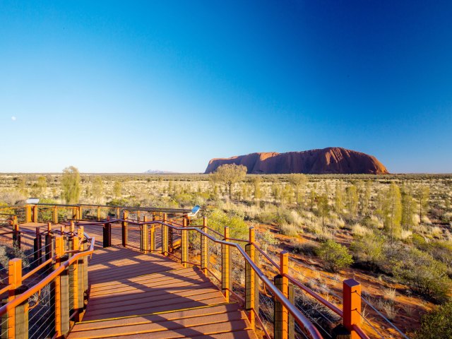 Wooden pathway leading across desert landscape to Australia's Uluru monolith