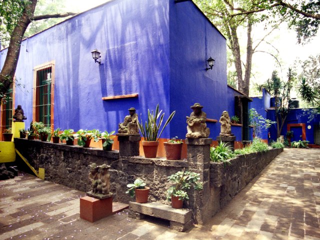 Blue exterior of Frida Kahlo Museum in Mexico City lined with plants and statues