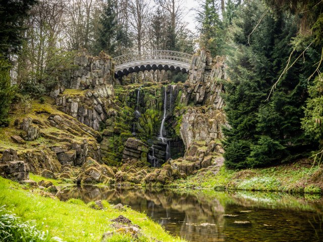 Bridge over waterfall and verdant landscape in Germany's Bergpark Wilhelmshöhe