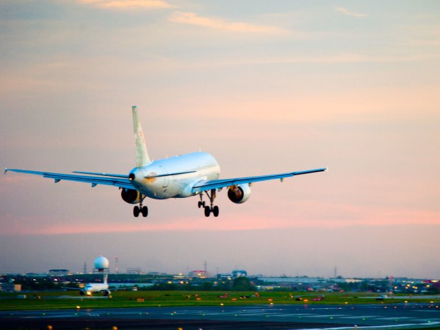 Airplane landing on runway at sunset, seen from behind