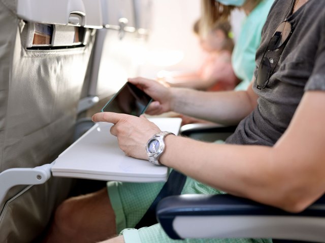 Close-up of passenger in airplane seat viewing phone with arms resting on tray table