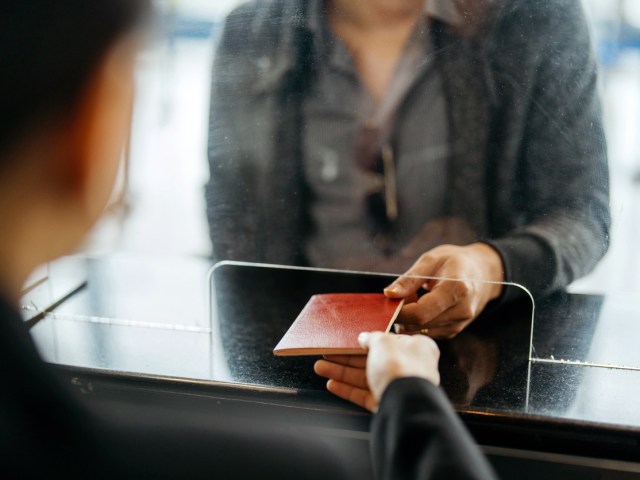 Close-up of person handing passport to inspection officer behind plexiglass