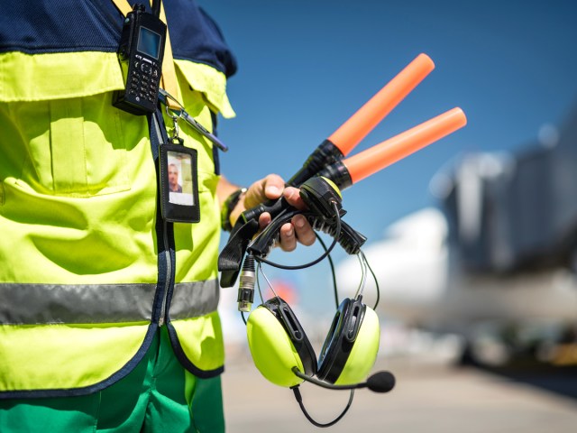 Close-up view of airport ramp agent holding orange batons to guide aircraft