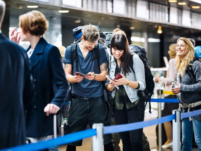 Two passengers standing in airport queue looking at their passports