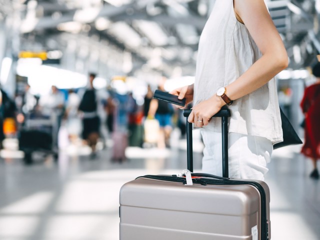 Passenger holding passport and suitcase in airport check-in hall