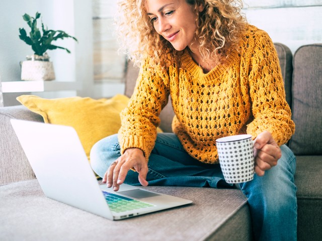 Person sitting on couch with coffee scrolling laptop 