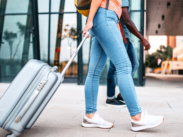 Person wearing sneakers rolling suitcase