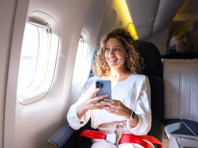 Passenger holding cell phone looking out airplane window