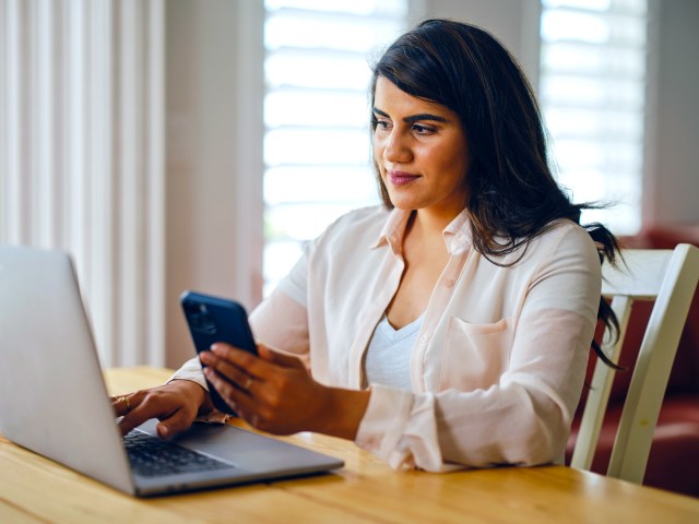 Person sitting at desk using laptop computer and cellphone