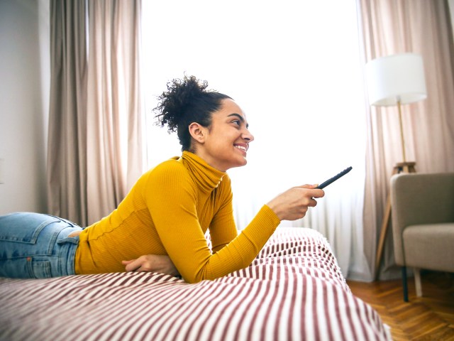 Hotel guest laying on bed using TV remote