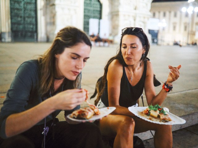 Two people sitting and eating on city sidewalk