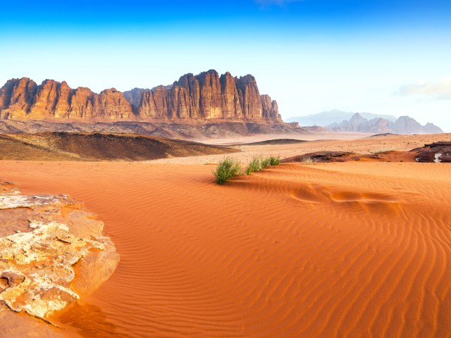 Sweeping sand dunes and towering rock formations in the distance in Wadi Rum, Jordan