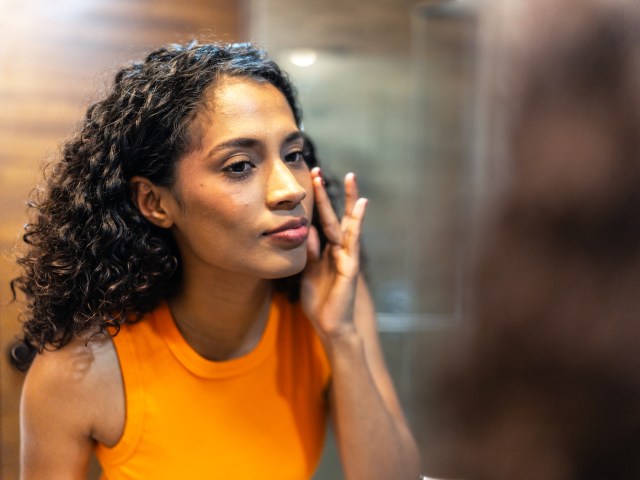 Person apply sunscreen to face while looking at mirror