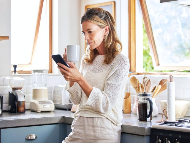 Person reading cellphone and drinking coffee in kitchen