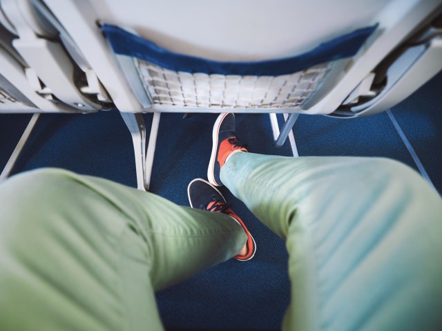 View of passenger's leg under airplane seat in front