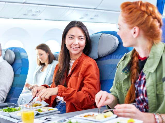 Two people on airplane eating in-flight meal