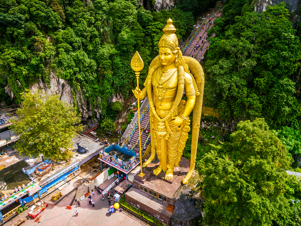 Giant golden statue of the Hindu deity Lord Murugan at entrance to the Batu Caves staircase in Malaysia, seen from above