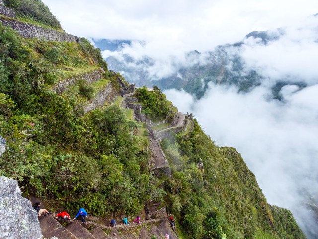 Climbers on Huayna Picchu Stairs overlooking cloud-covered Machu Picchu in Peru