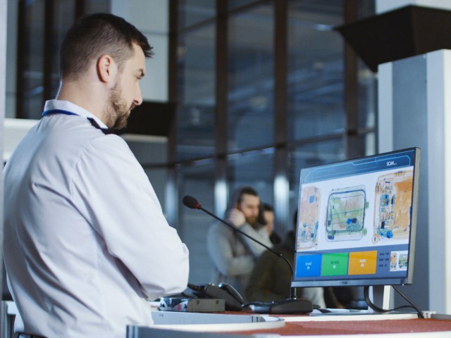 Airport security officer viewing X-ray images of travelers' luggage at security screening station