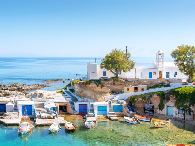 Boats in marina beside traditional white homes on island of Milos, Greece