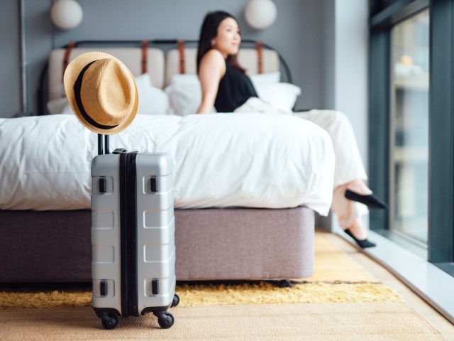 Hotel guest sitting on bed next to suitcase