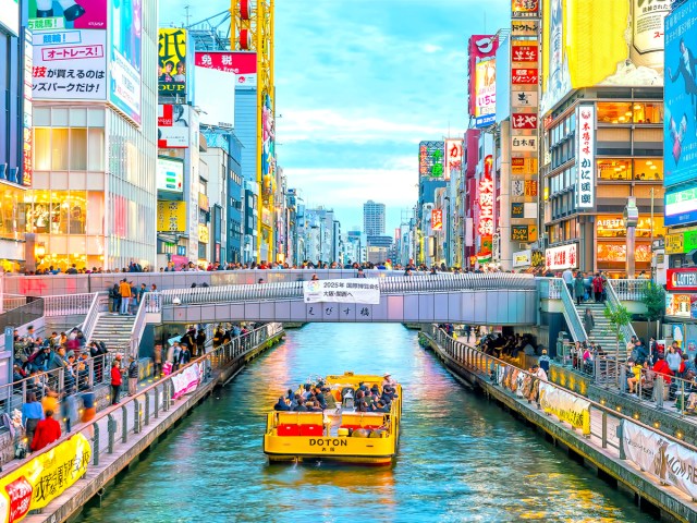 Boat cruising on river through busy downtown Osaka, Japan