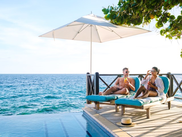 Couple relaxing by pool and ocean under umbrella