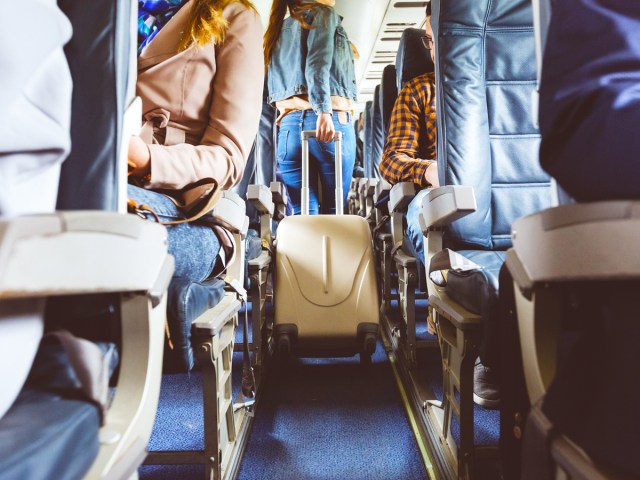 Airline passenger rolling suitcase through airplane aisle