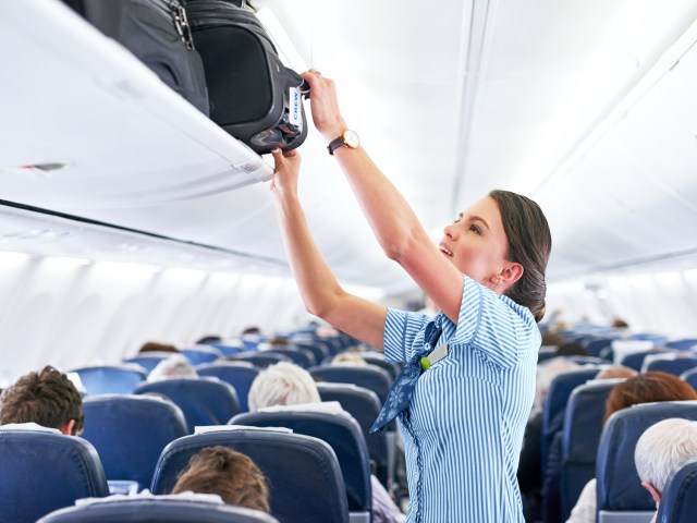 Flight attendant stowing luggage in overhead compartment