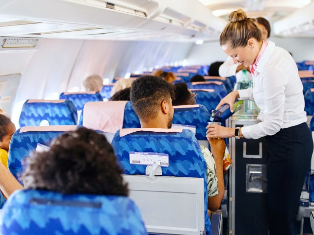 Flight attendants in aircraft aisle pouring beverages for passengers