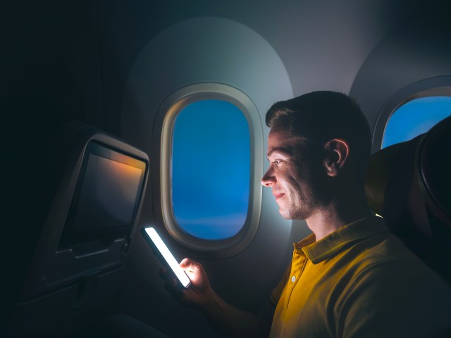 Passenger on night flight looking at phone