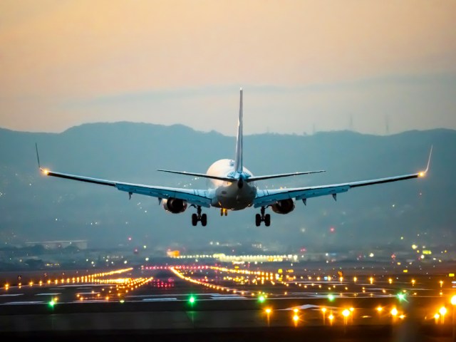 Commercial aircraft landing on lighted airport runway at dusk