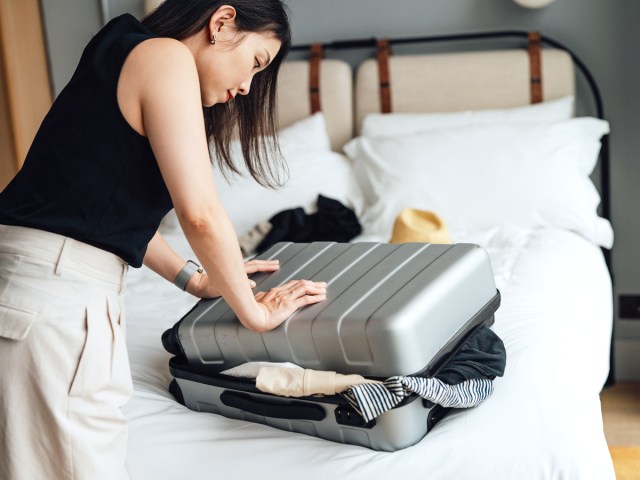 Traveler trying to close overstuffed suitcase