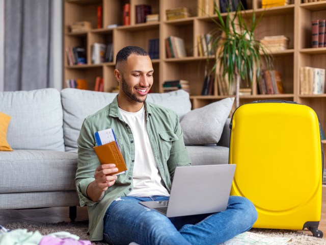 Person holding passport and ticket while looking at laptop computer