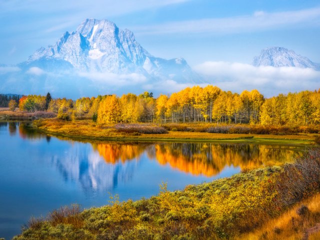 Trees in autumn reflecting on lake with mountains in background in Jackson Hole, Wyoming