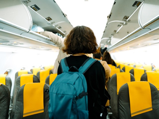 Passengers walking through narrow-body aircraft aisle to their seats