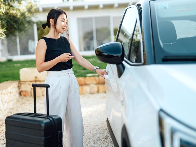 Woman with suitcase opening rental car door