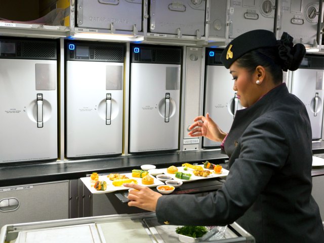 Qatar Airways flight attendant preparing meals in aircraft galley