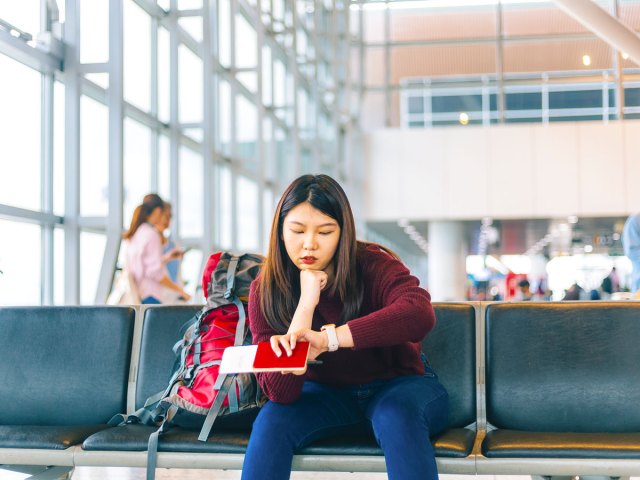Traveler holding passport and boarding pass sitting in airport terminal