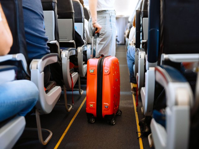 Passenger rolling suitcase through aircraft aisle