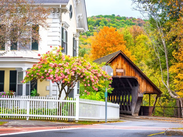 Home next to covered bridge surrounded by fall foliage in Vermont