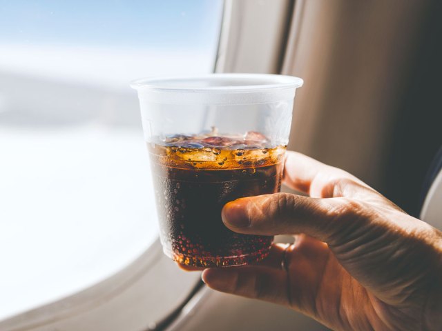 Passenger holding cup of soda in front of airplane window