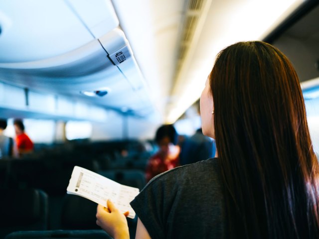 Passenger holding boarding pass looking for seat on plane