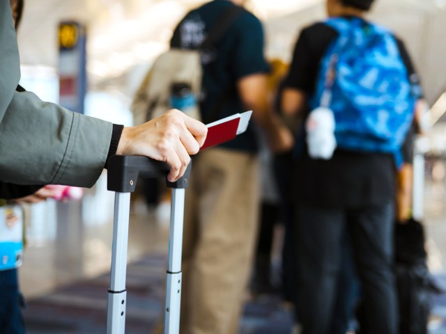 Traveler holding suitcase with boarding pass and passport in hand