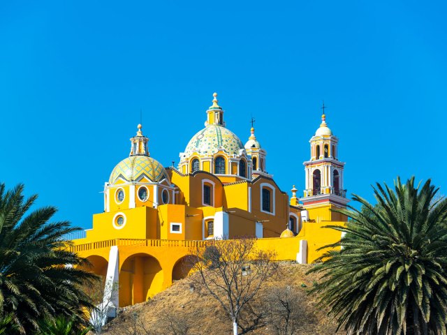 Yellow church framed by palm trees in Cholula, Mexico